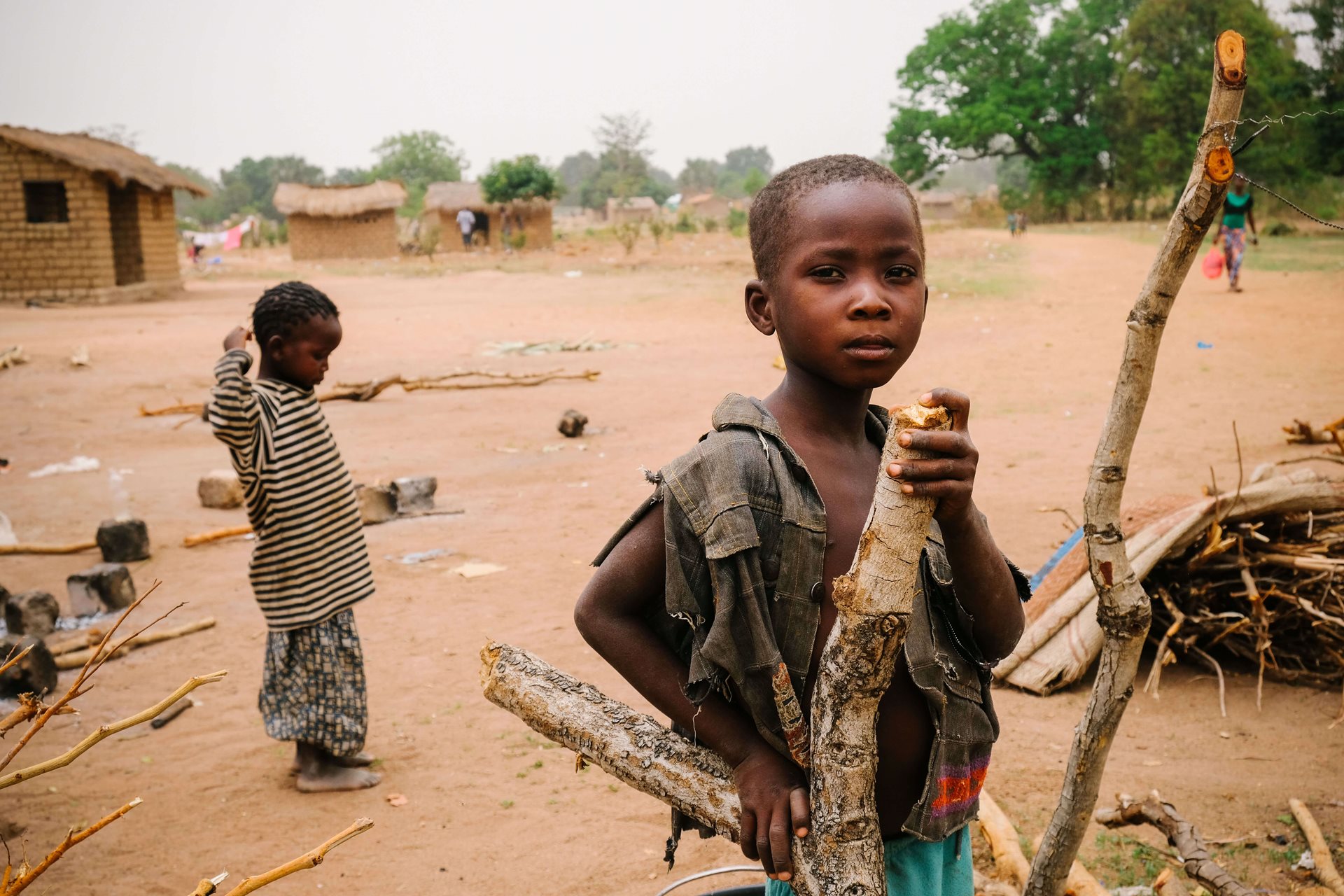 A child holding a tree limb next to a pile of sticks.
