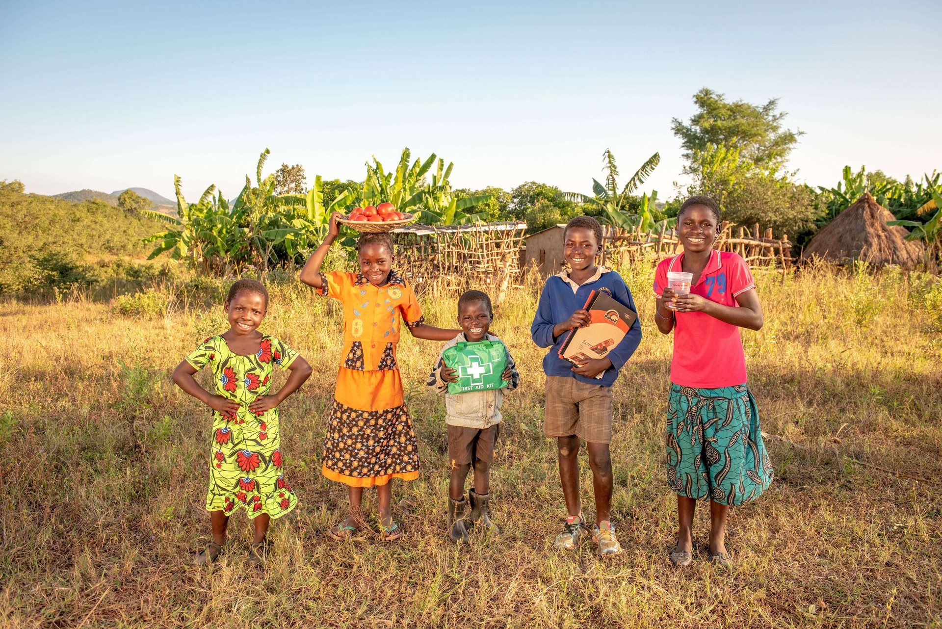 A group of children standing in a field holding essential items.