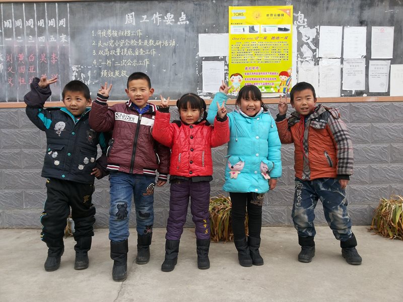 Five children from China pose with their brand new winter boots in front of a blackboard.