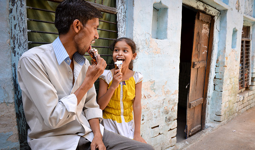 In India a dad and his young daughter sit outside a building eating ice cream cones