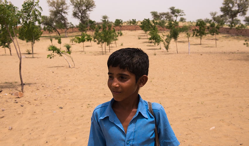 A young boy walks through a desert-region in India, on his way to school. It is dry and sandy.
