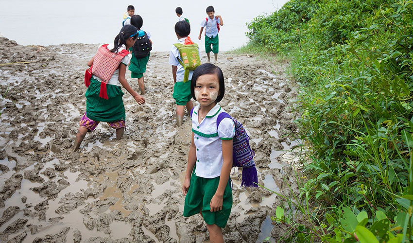 A group of school children prepare to cross a riverbank on their way to school in Myanmar.