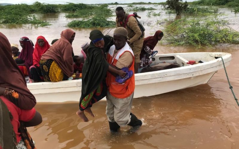 A man lifts a woman from a small boat floating on floodwaters, to carry her to high ground.