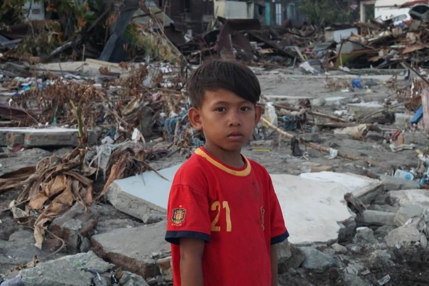 In Indonesia, a boy stands in front of the earthquake-tsunami devastation in his community.