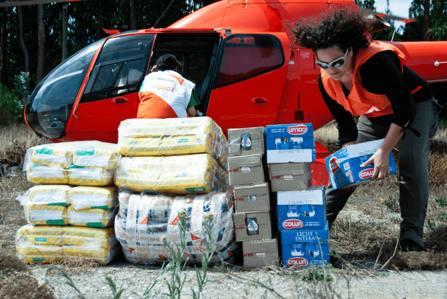 Two people in orange World Vision vests unload earthquake relief supplies from a helicopter.