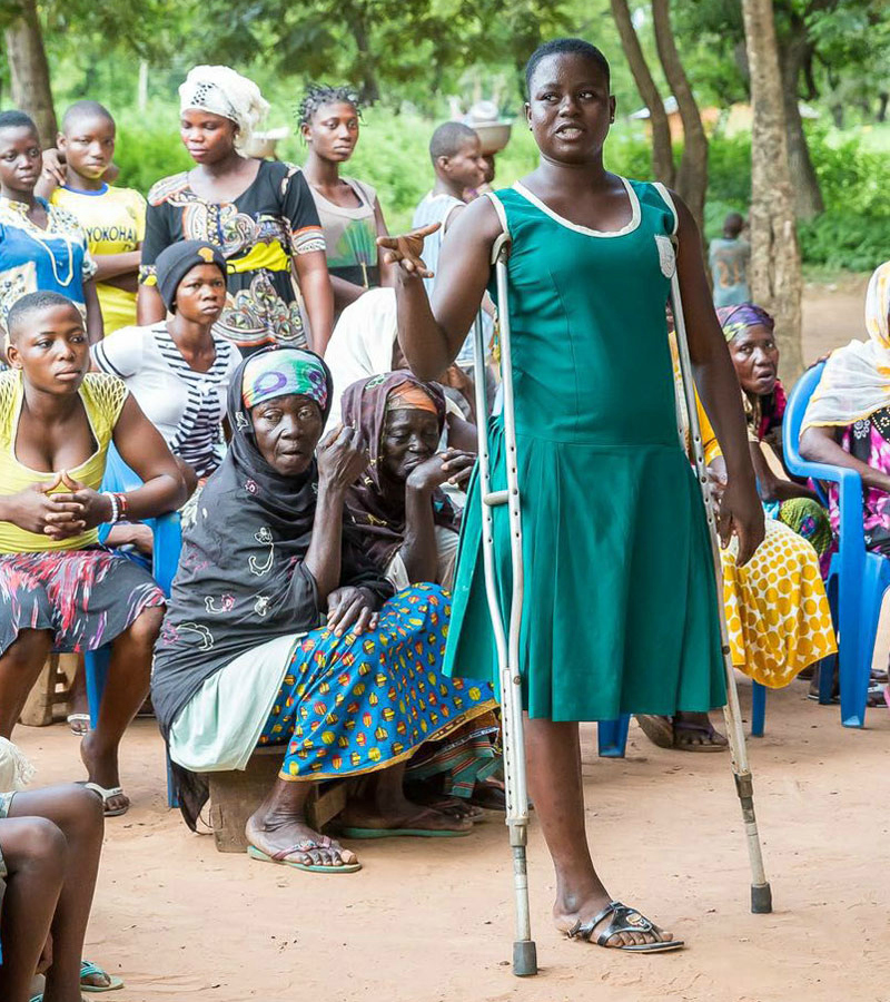 A young woman with crutches stands in front of a group of women in Ghana.