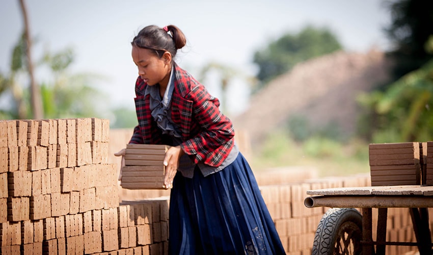 In Cambodia a girl packs clay bricks in a wall formation in the hot sun