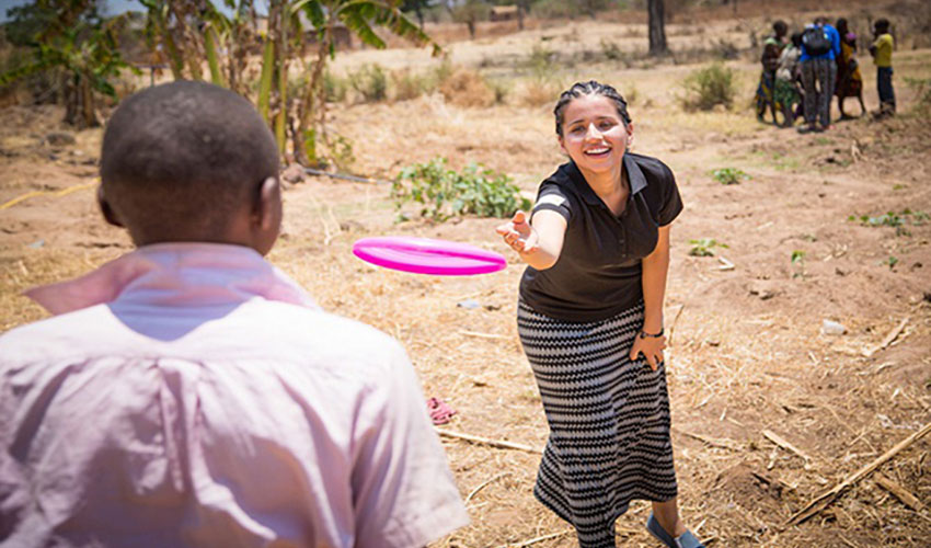 A Canadian woman and Tanzanian boy throw a frisbee back and forth in a Tanzanian village.