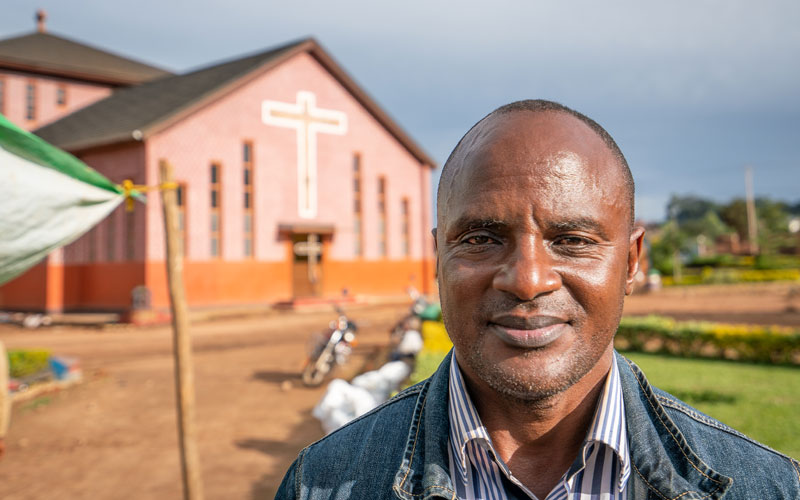 a Congolese man stands in front of a church.