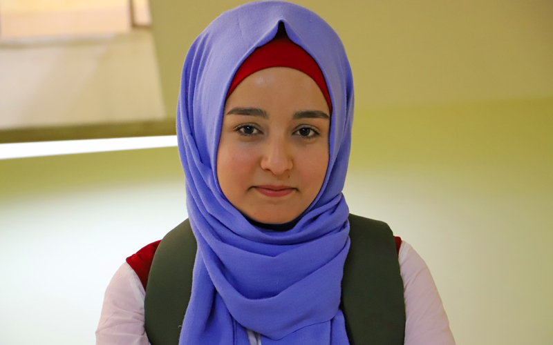a young woman wearing a head scarf stares straight into the camera.