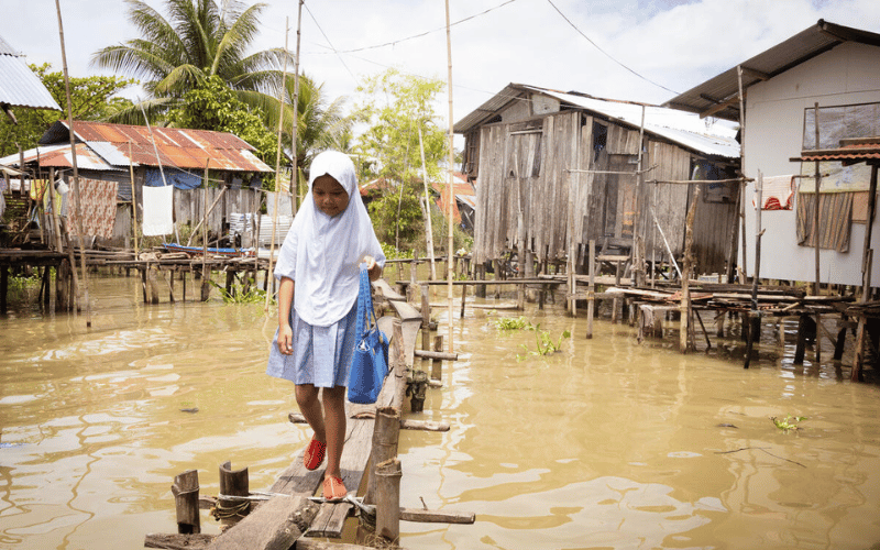 A young girl carrying a bag walks along a raised platform above floodwaters.