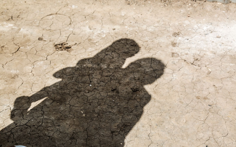 shadow of an adult holding a small child on a background of cracked earth