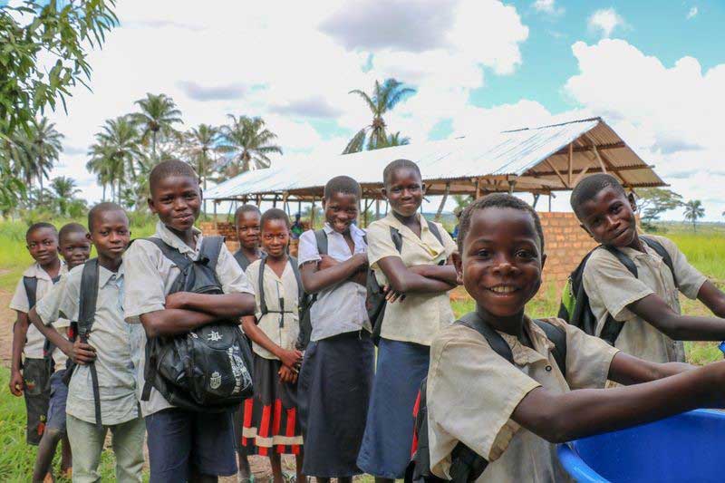 Children in simple uniforms stand outside their newly rebuild school. They are looking content, and some, even happy.