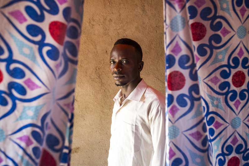A man from the DRC stands in between colourful curtains.