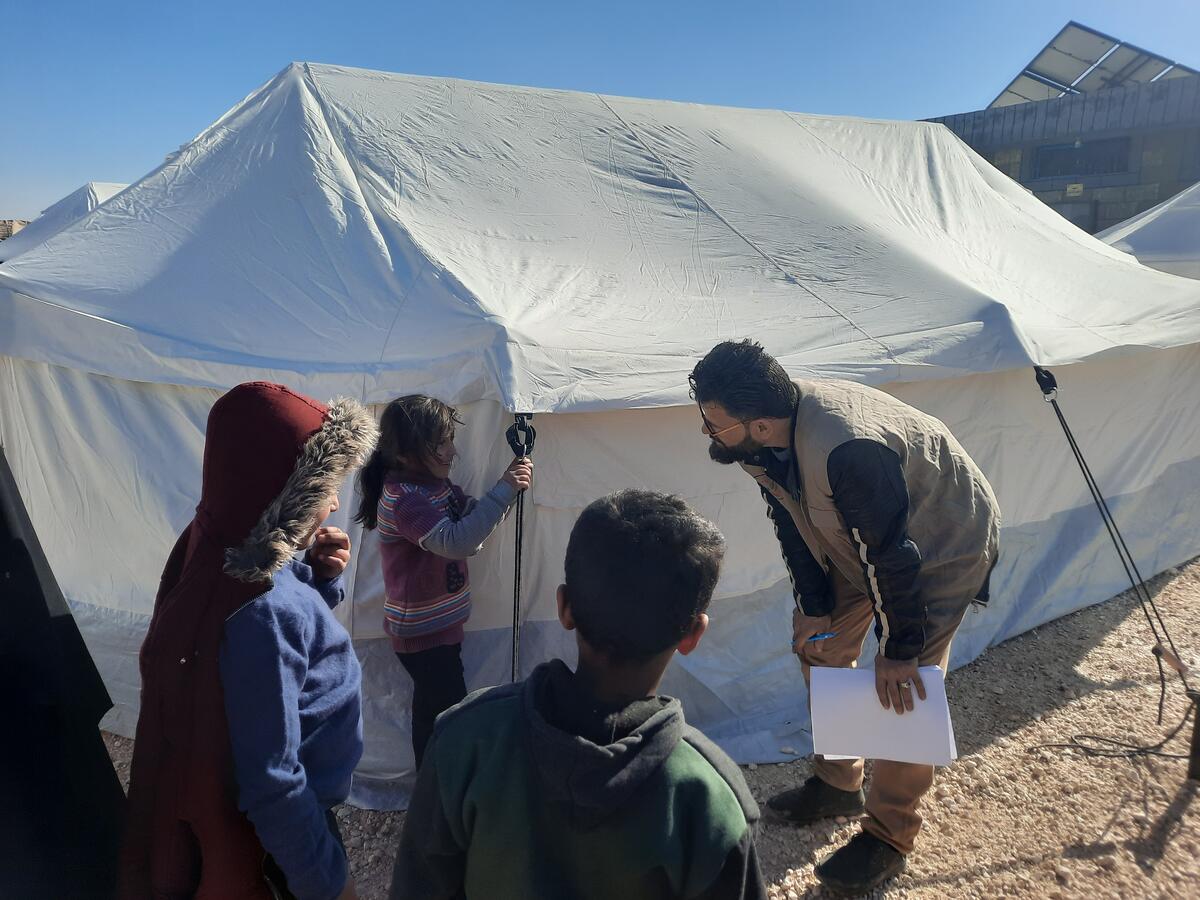 In Syria, an aid worker talks to three children outside of their tent shelter.
