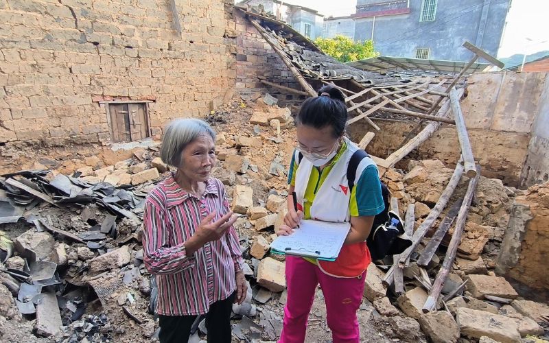 In China, a World Vision worker takes notes while a woman speaks. They are standing amidst rubble.