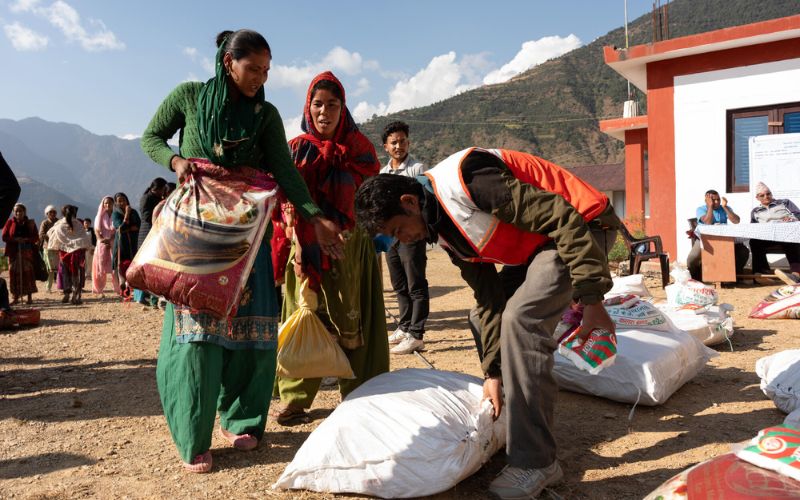 A man in a World Vision vest passes emergency grain sacks to people lining up in a mountainous setting.