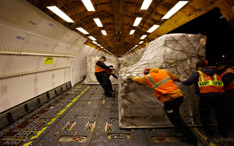 People push flats of emergency food supplies onto a cargo plane.