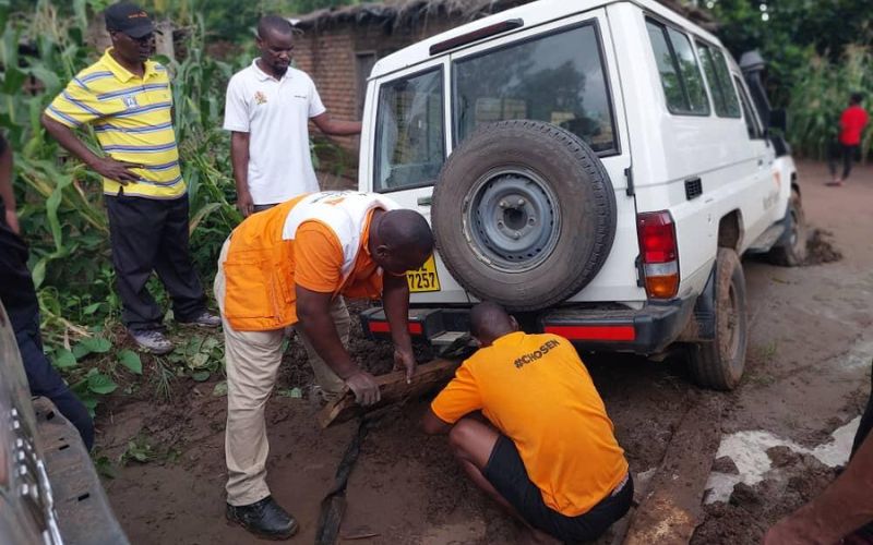 World Vision workers wedge a truck sinking in mud on a hillside to lift it up.