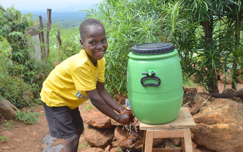 a young Kenyan boy smiles as he washes his hands with clean water from a jug.
