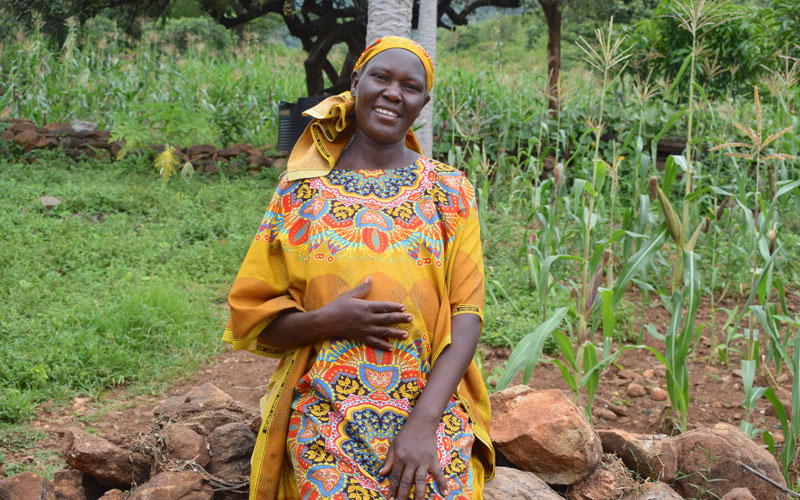 a Kenyan woman smiles at the camera and holds her pregnant belly