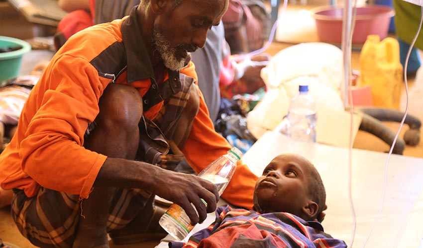 A man feeds water to a child who is sick and being treated for severe malnutrition in East Africa..