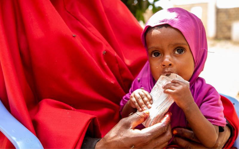 A very young girl in Baidoa, Somalia, is held in a woman’s arms as she’s fed food to combat severe malnutrition.