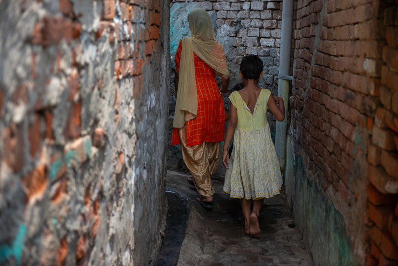 A woman and a young girl walk through an alley, away from the camera.