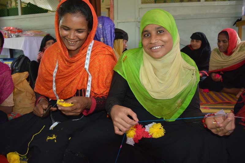 Two Rohingya refugee women sewing in a room full of women.