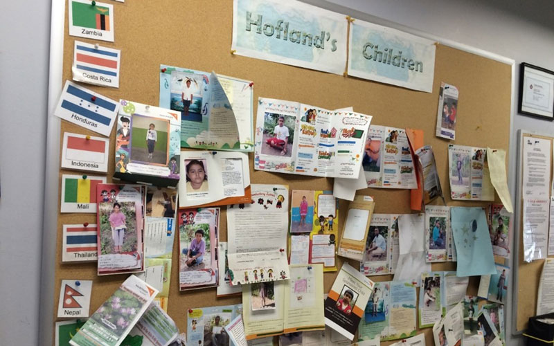 A large bulletin board reading “Hofland’s Children” is covered with picture folders showing children’s faces.