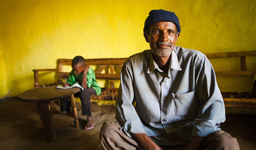 In Ethiopia, a father sits in a classroom while his son studies in the background