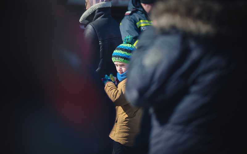 In Romania, a little child warmly dressed stand amidst a crowd of adults wearing black.