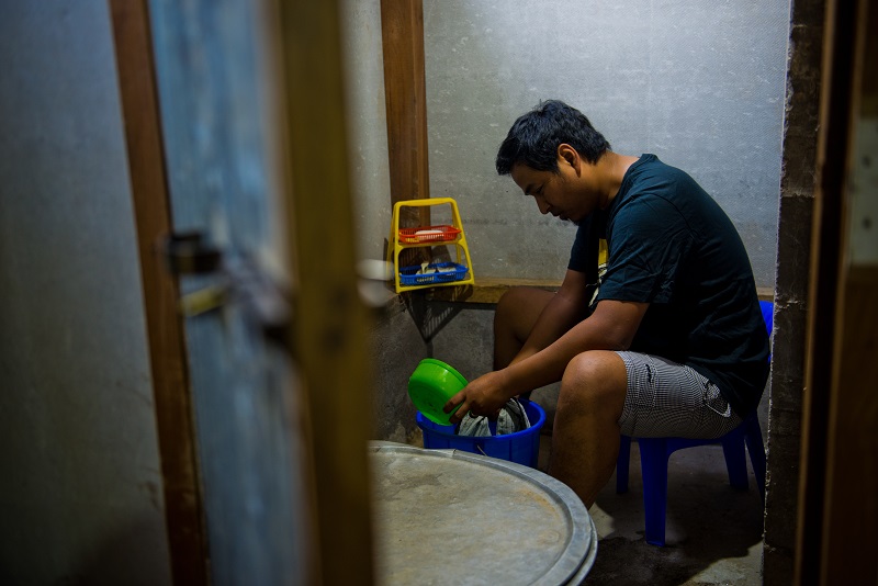 A man washes his dishes in a bucket.