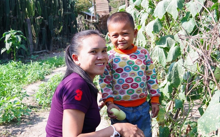 A woman smiles with a kid in a vegetable garden.