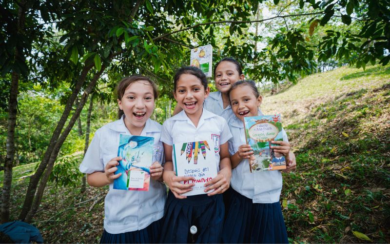 Four Honduran girls smile widely while holding new books.