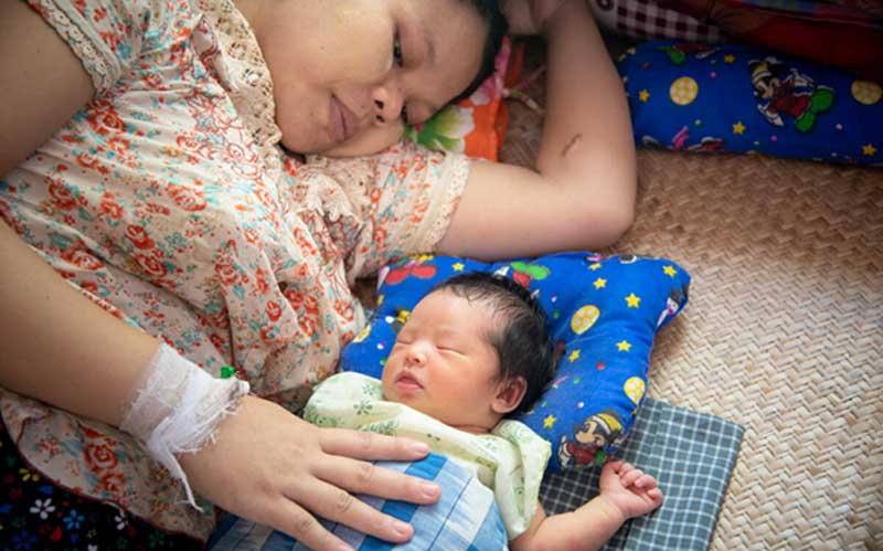In Myanmar, a mother and her newborn baby lie together, with pillows, on a woven mat.