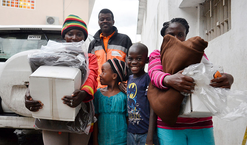 Two women hold bundles beside two smiling children and a man in a World Vision jacket