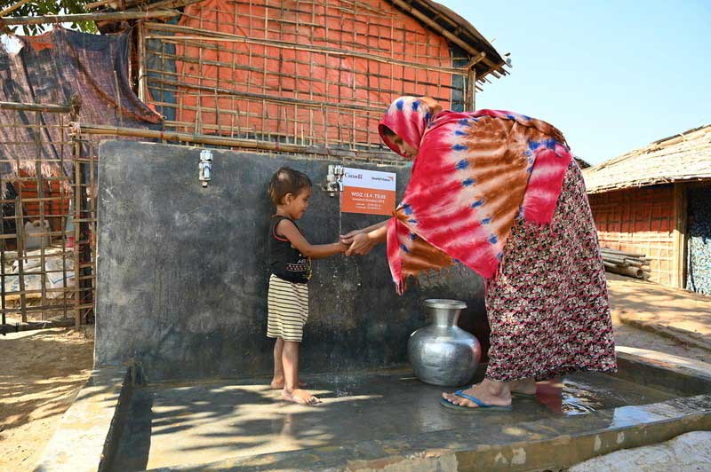 A woman wearing a colourful headscarf helps a little boy wash his hands at a public tap installed by World Vision.