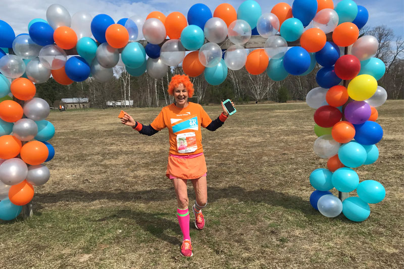 a woman wears orange and runs through a balloon archway