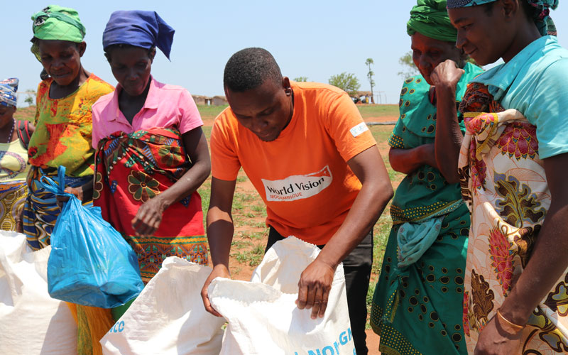 a World Vision Mozambique staff person distributes emergency food aid to a group of women survivors of Cyclone Idai