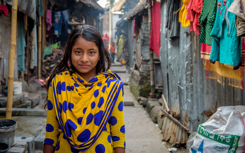 A young girl from Bangladesh stands in the alley outside of the shanty her family calls home.