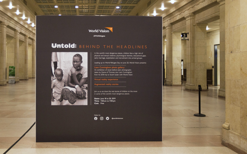a dark grey wall with a photo of a young black woman and a toddler next to her and text describing an event called Untold: Behind the Headlines, commemorating World Refugee Day