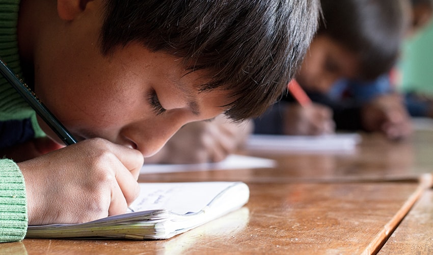 Extreme close up of boy writing at a desk in school, in Peru.