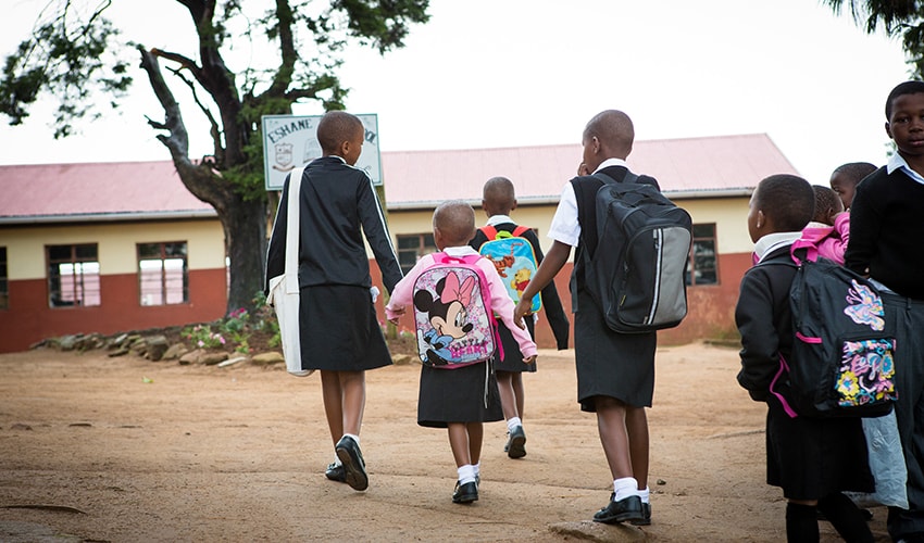 A group of children hold hands and head to their school in South Africa