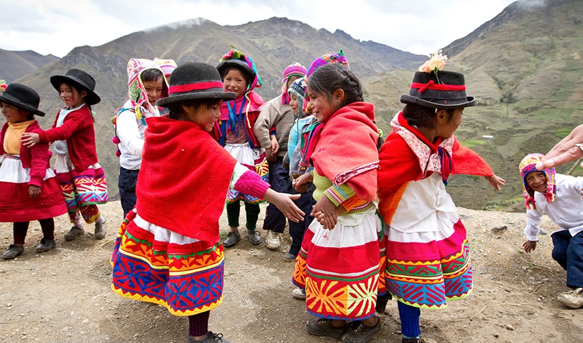 On a mountain in Peru, a group of children wearing traditional dress dance together.
