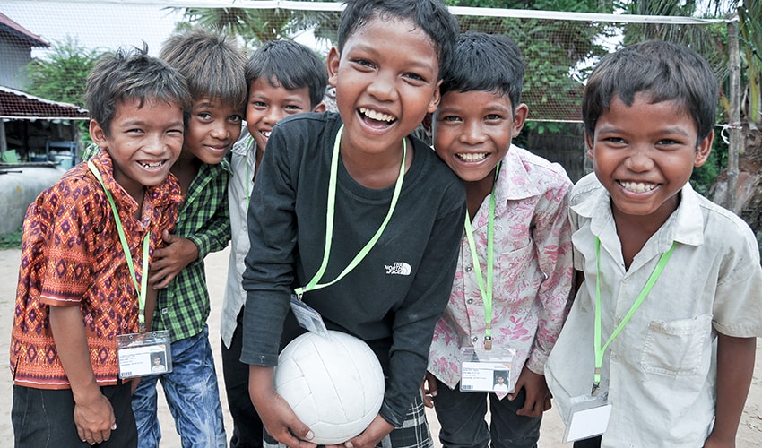 6 Cambodian boys laugh together, while the child in the middle holds a soccer ball.