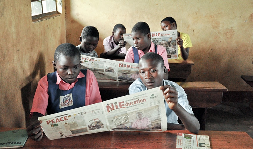 Students sit in their Ugandan classroom and read their local paper in pairs.