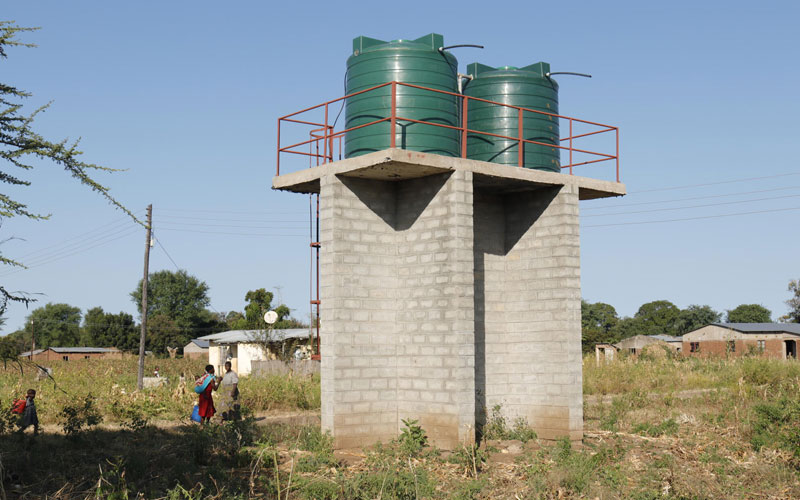 A tall water storage structure outside in the middle of a grass field.  
