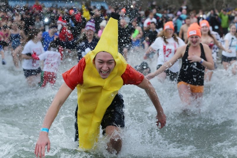A guy in a banana suit run into a lake while a crowd is behind him.