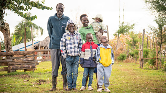 A family of six standing together in a rural area, all smiling widely.